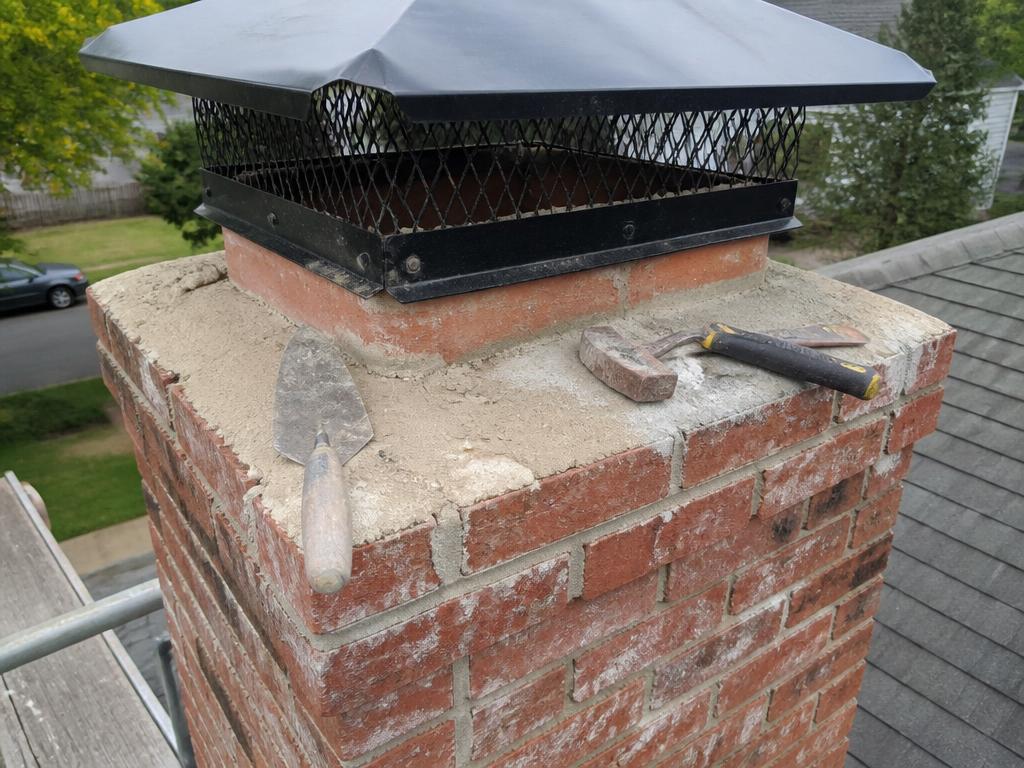 Brick chimney crown and metal chimney cap with masonry tools during repair